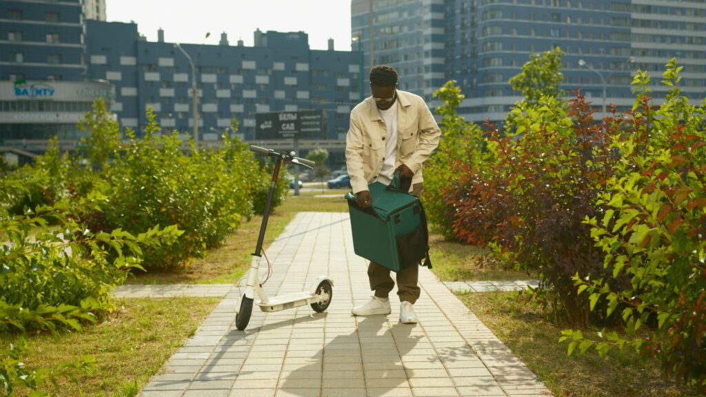 A delivery man with a package readies his scooter for urban delivery in a city setting.