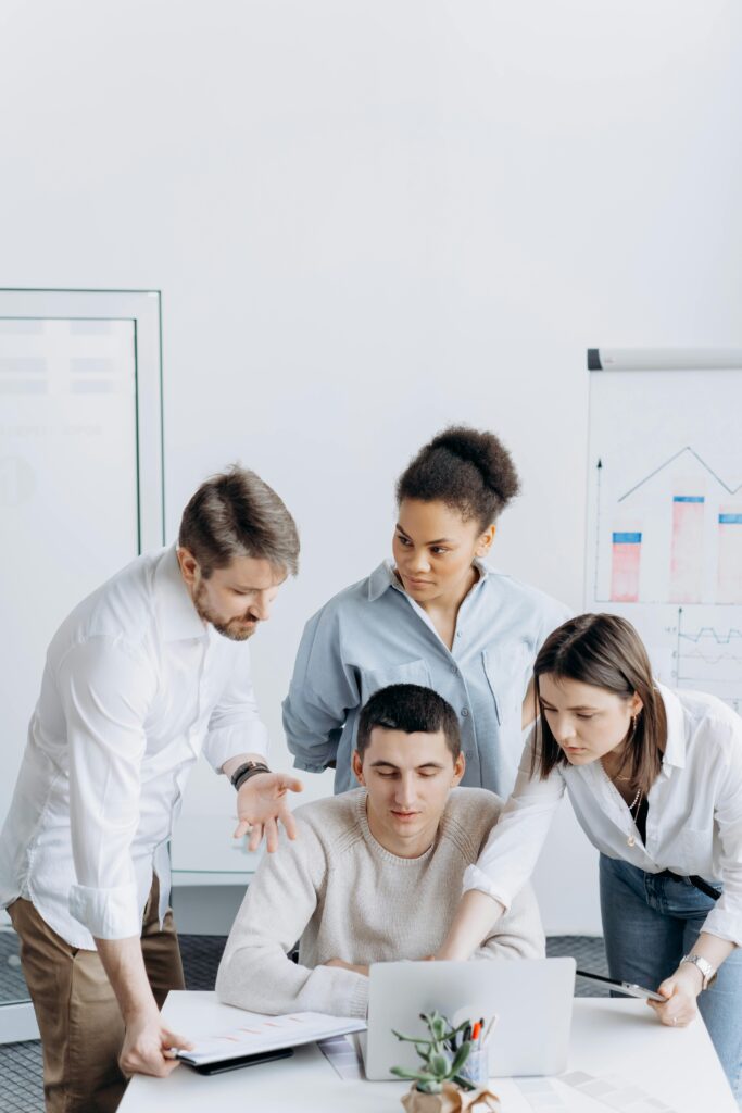 A diverse group of coworkers gathered around a laptop discussing an office project.